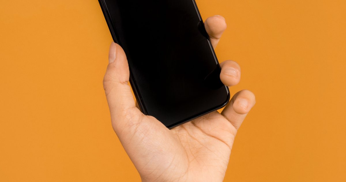 A hand holding a smartphone against a plain orange background