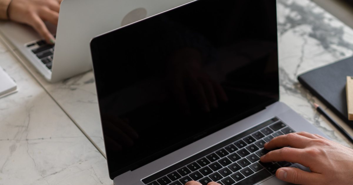 A MacBook open on a marble desk with hands at the keyboard