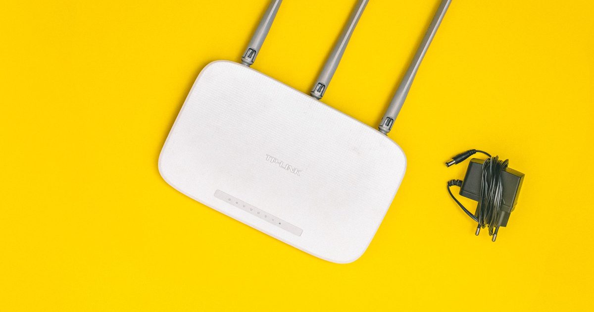 A white TP-Link wireless router with three antennas, lying beside its power adapter