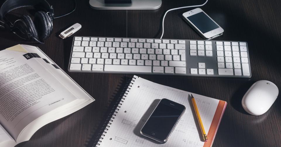 A desk with an open notebook, a keyboard and two smartphones