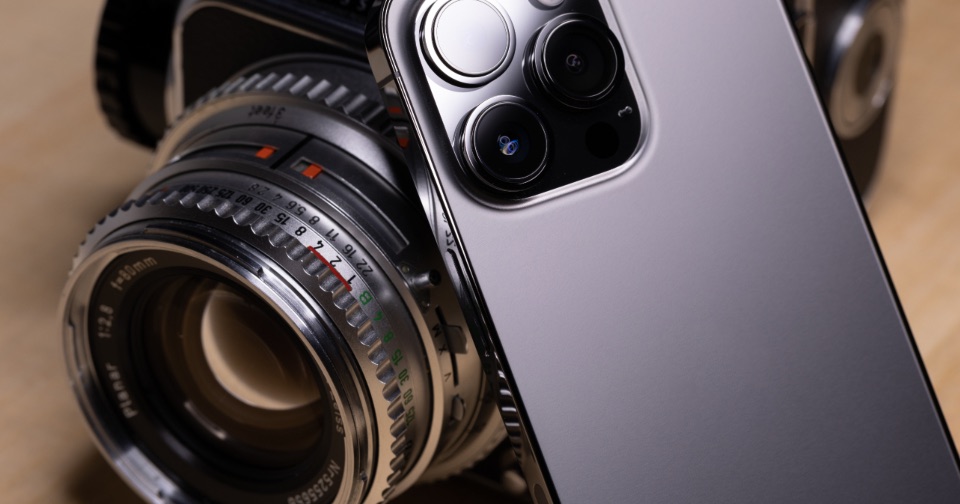 The camera lenses on the back of a smartphone, propped against an old film camera lens